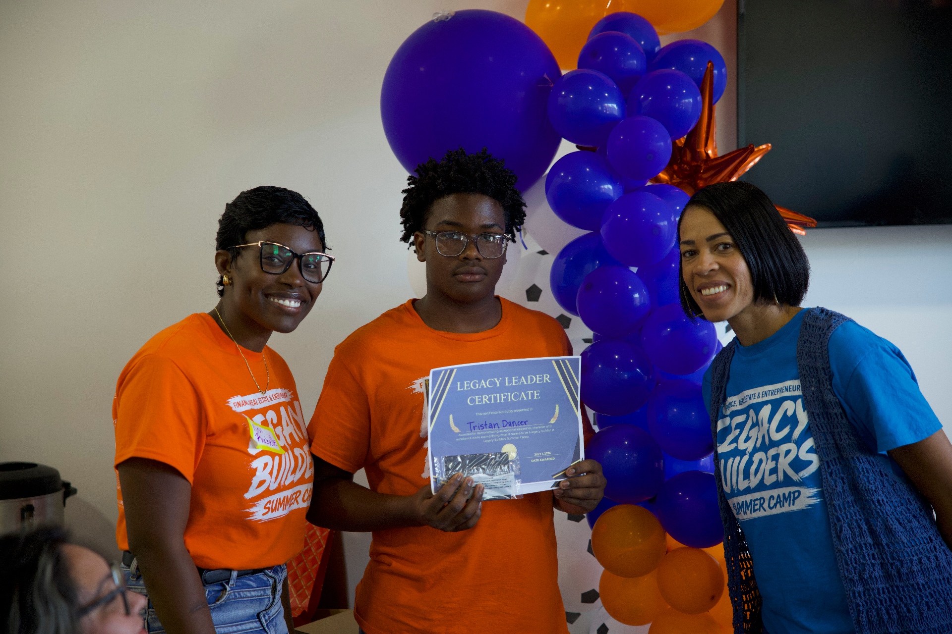 An Academy student receiving a Legacy Leader certificate alongside two mentors